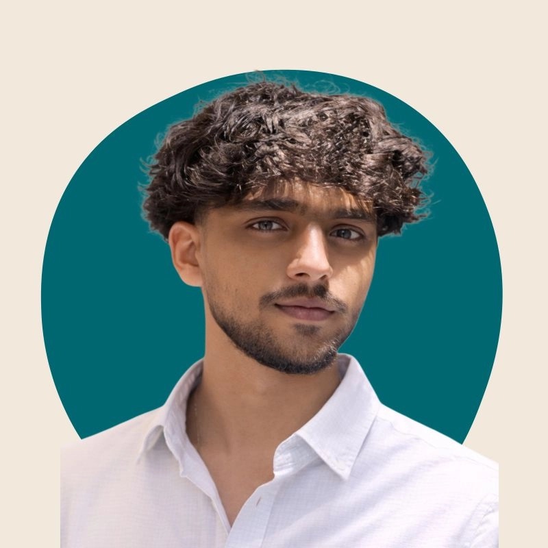 “Portrait of a young man with curly hair and trimmed beard wearing a white shirt against a teal circular background”
